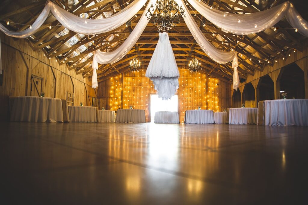 Wedding venue interior with draped fabric, chandeliers, and tables.