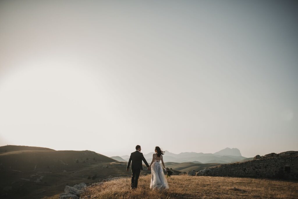 Newlyweds walk hand-in-hand through a field at sunset, qualify wedding venue leads